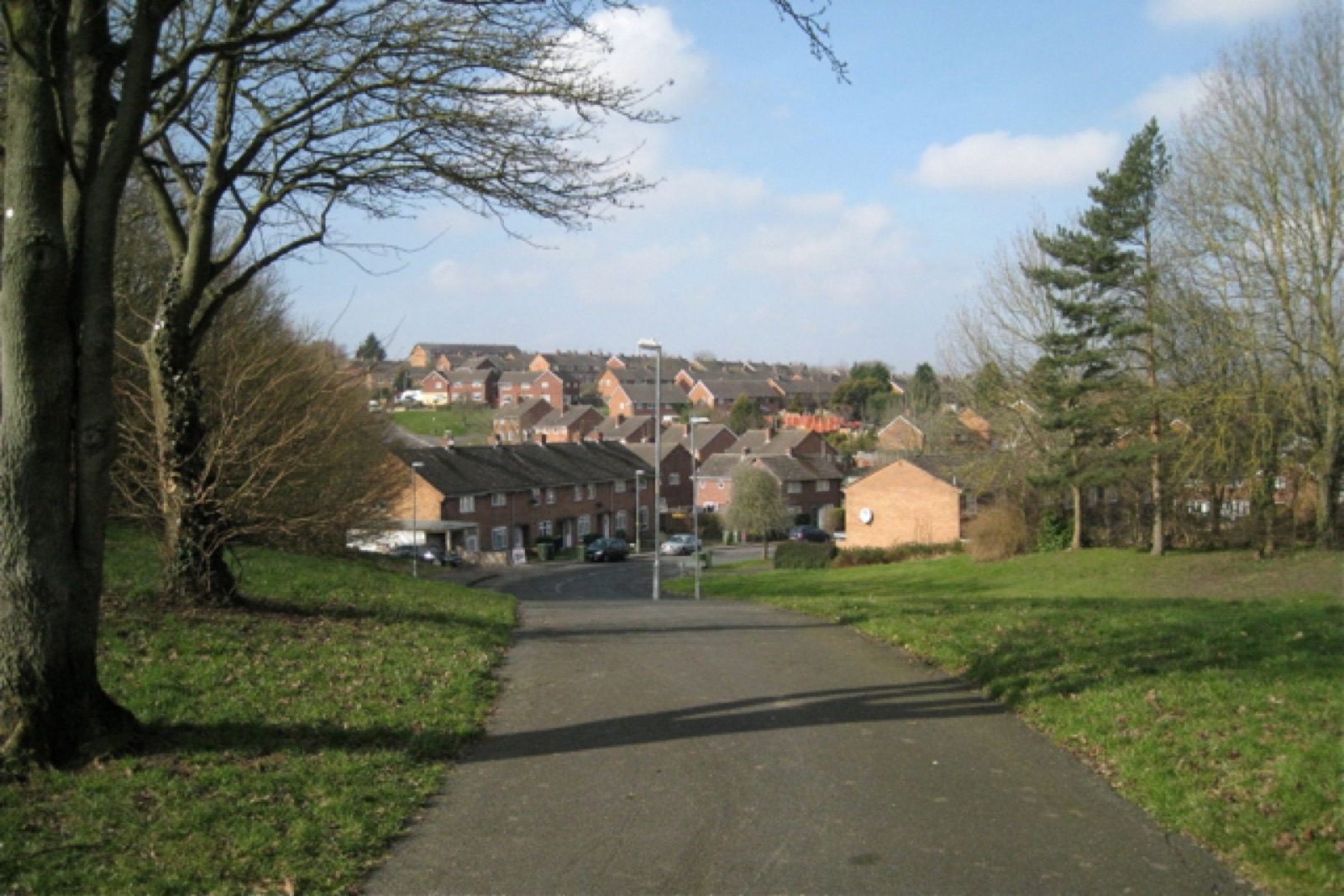 A path through grass and trees, looking towards houses in Woodrow